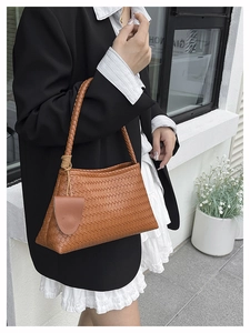 Detail of woven leather shoulder bag with circular charm against a minimalist background