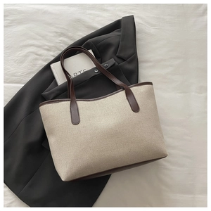Canvas tote bag detail showing contrast brown leather straps on a beige canvas surface