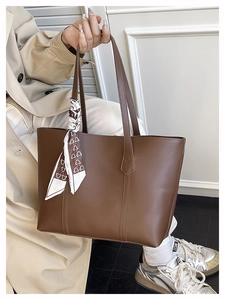 Detail of a brown tote bag with long handles and a heart pattern scarf for daily use