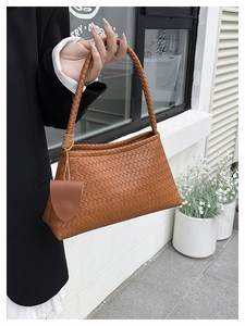 Detail of woven brown leather handbag featuring a braided handle and matching mini pouch