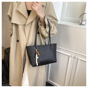 Detail of black woven texture tote bag with wooden bead charm and long shoulder strap