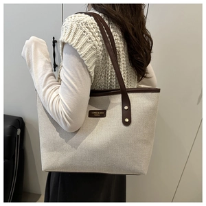 Detailed side view of off-white canvas tote bag with brown leather straps and brand logo
