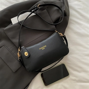 Fashionable black lychee leather crescent shoulder bag with golden hardware on white fabric