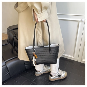 Detail of black woven tote bag with beaded tassel charm held by a model in a minimal room