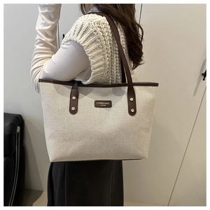Detail of cream canvas tote bag with brown leather handles worn by model for daily commute