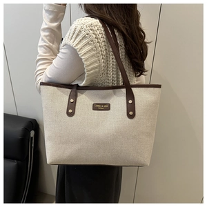 Detail of canvas tote bag with brown leather handles and logo on a shoulder-carried model