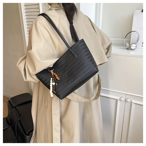 Detail of black woven tote bag with wooden bead charm on a khaki trench coat background