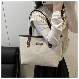 Close-up of beige canvas tote with dark brown leather trim and metal brand plaque