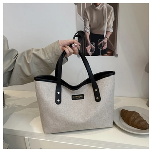 Close-up of contrast canvas tote bag featuring premium leather trim and gold brand logo