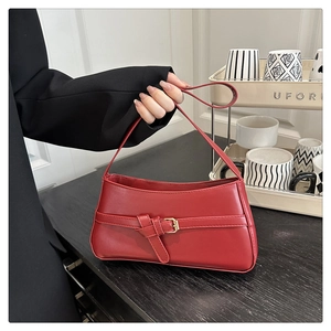 Detail of red faux leather shoulder bag featuring a gold buckle and matte finish