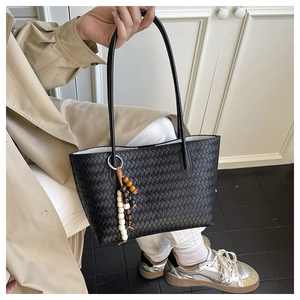 Close-up of black woven tote bag with wooden bead charm on a person in khaki trench coat