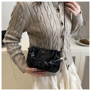 Détail d'un sac nuage plissé noir avec bandoulière chaîne dorée et logo de la marque