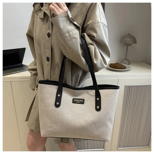 Detail of a large color-block canvas tote bag with black leather straps and brand label