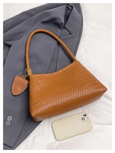 Detailed view of brown woven hobo bag with matching leather tag on gray suit background