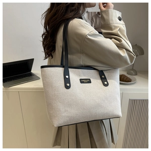 Close-up of cream canvas tote bag with black leather straps in a cozy office setting