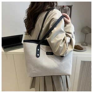 Close-up of stylish canvas tote bag with black strap and logo label on a beige lamp background