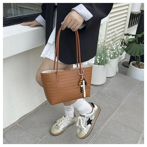 Detail of woven brown tote bag with Intrecciato pattern and bohemian beaded charm