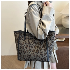 Detailed view of leopard print canvas tote bag with black leather straps in warm interior