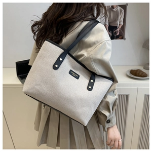 Detail of beige canvas tote bag with black leather straps and brand logo tag