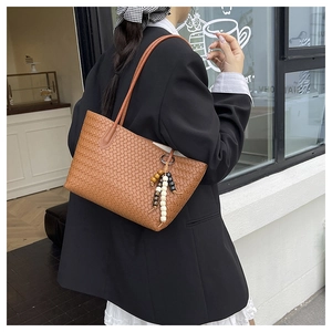 Detailed view of brown woven leather tote with beaded tassel charm on a shoulder strap