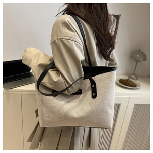Close-up of minimalist beige canvas tote bag with black leather trim and double handles