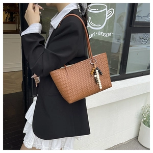 Close-up of brown woven tote bag with a colorful beaded tassel charm and slim handles