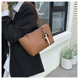 Detail of brown woven tote bag featuring ethnic wooden bead charm and long shoulder strap