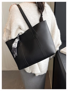 Detail of a large black matte leather tote bag with a decorative scarf on shoulder strap