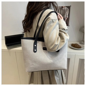 Detail view of canvas tote bag with black leather straps and brand label in home setting