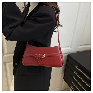 Detail of burgundy leather baguette bag with metal buckle worn over the shoulder