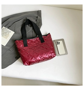 Macro detail of burgundy shiny tote bag with embossed pattern and black woven handles