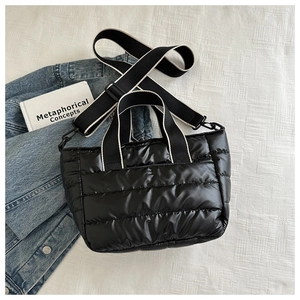 Detail of black quilted puffer tote bag with wide strap on light blue denim fabric