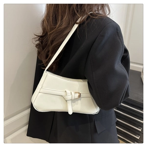 Detailed side view of white faux leather baguette bag with gold buckle on black blazer
