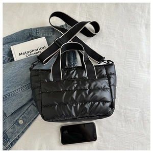 Quilted black puffer tote bag shown with smartphone for size scale and woven strap detail