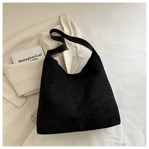 Detail of minimalist black suede hobo bag on blazer with book for urban office style