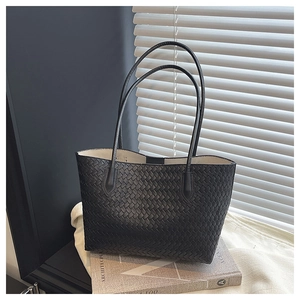 Close-up of black woven leather tote bag texture with long straps on a minimalist setting