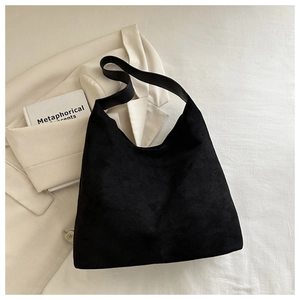 Overhead shot of black matte suede tote bag with wide strap on minimalist white blazer