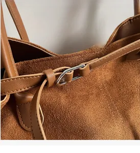 Detail of silver U-shaped metal clasp on brown suede tote bag with leather straps
