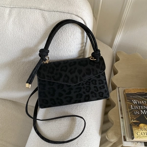 Sac à main noir à motif léopard avec poignée nouée et détails dorés sur un canapé