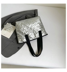 Detail of silver metallic tote bag featuring embossed bow patterns and black web handles