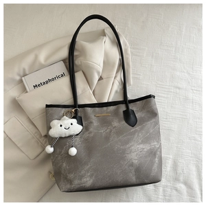 Sac cabas gris texturé avec breloque nuage, disposé sur une veste de costume beige