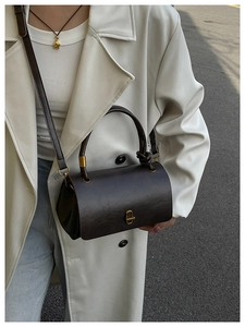 Close-up of retro dark brown cylinder crossbody bag with golden metal buckles