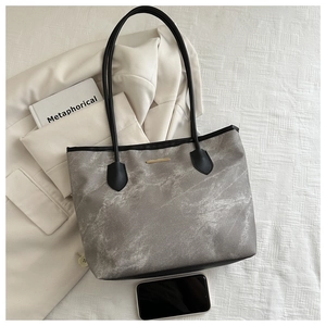 Détail d'un cabas gris marbré avec anses noires et une plaque métallique dorée chic