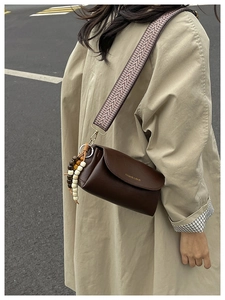 Dettaglio borsa vintage in pelle marrone con tracolla geometrica e ciondolo in legno