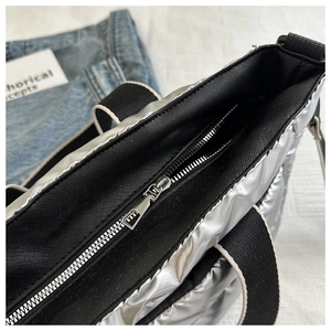 Detailed close-up of the black metal zipper and interior lining of the silver quilted tote bag