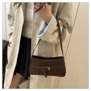Detail of a dark brown shoulder bag with a gold metal buckle and leather-like texture