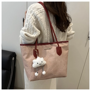 Detail of a pink pebble texture tote bag featuring red leather handles and a plush cloud charm
