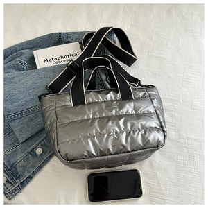 Overhead view of a silver quilted puffer tote bag with striped straps and denim accessory