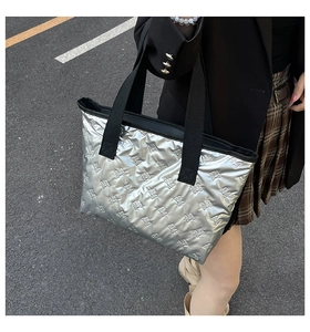 Detail of silver metallic tote bag featuring embossed bow patterns and black web handles