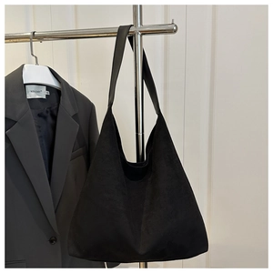 Detail of a black suede tote bag with a wide shoulder strap hanging on a metal rack